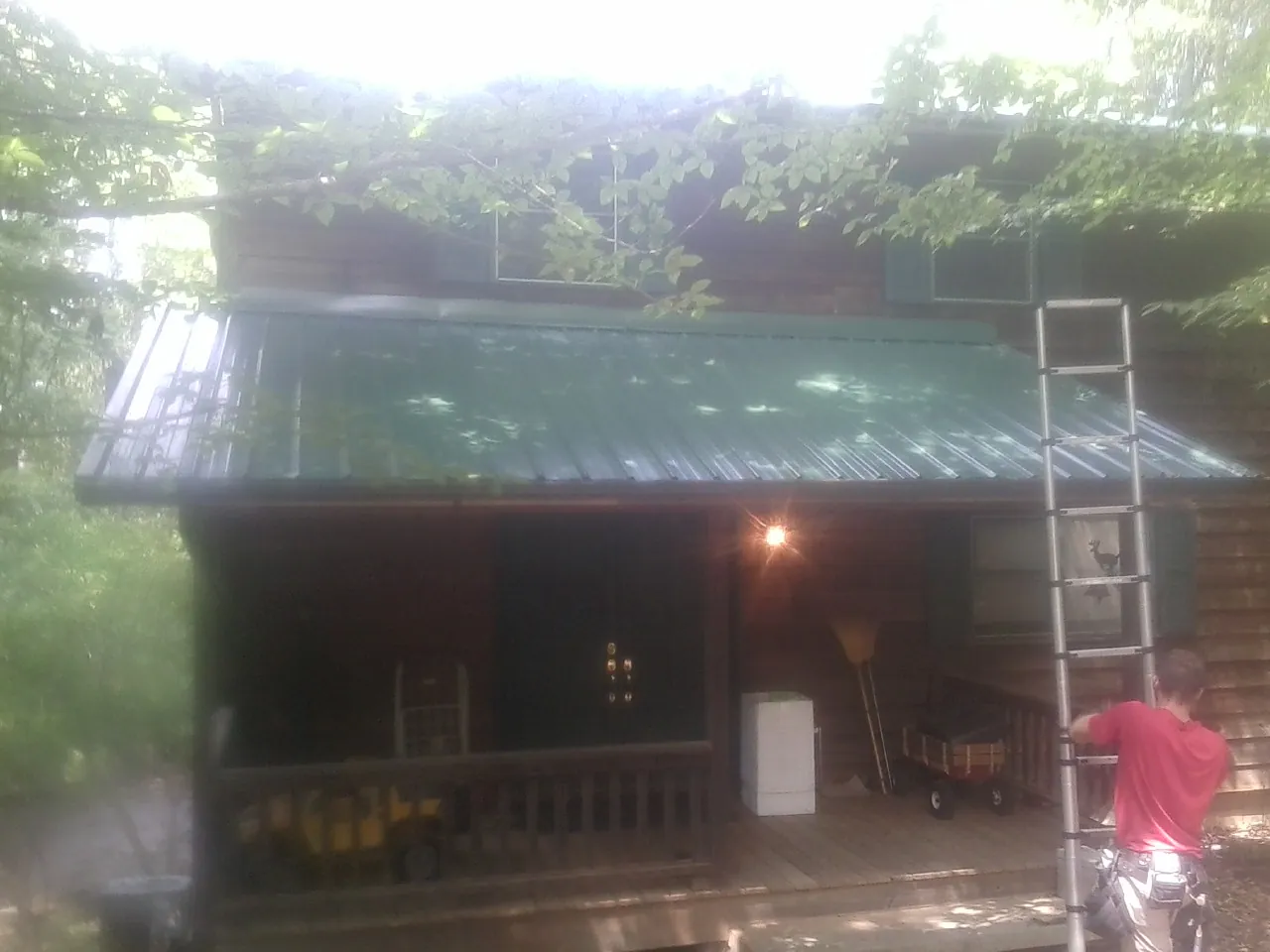 Worker on a ladder at the green porch roof of a wooded cabin in Palmyra